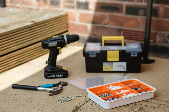 a drill, black tool box and orange nail and screw organizer