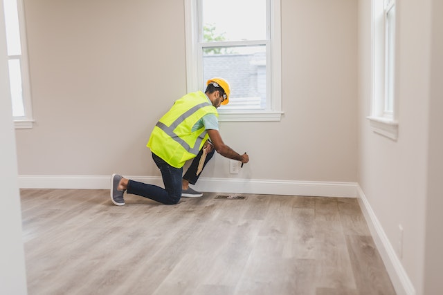 property inspector in a reflective vest and hard hat using a flashlight to checks a home's vents