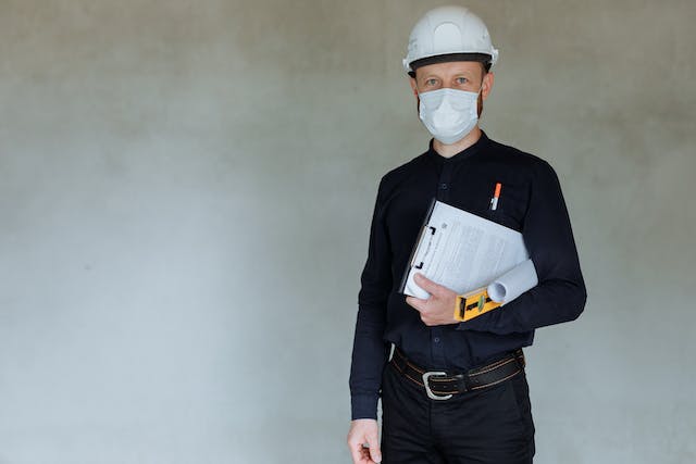 home inspector in a hard hat and mask holding an inspection report